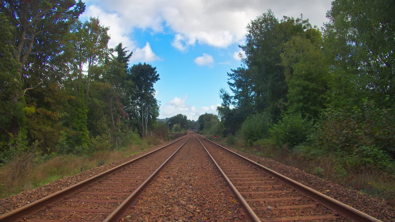 vía de tren vacía entre árboles verdes bajo un cielo azul con nubes blancas rodantes durante el día