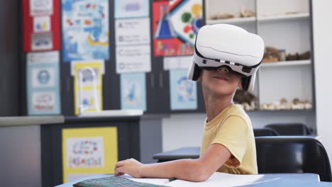 biracial boy wearing a vr headset sits at a school desk with copy space, in a classroom at school