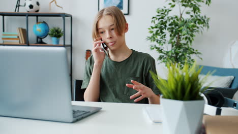 teenage boy talking on phone while using laptop