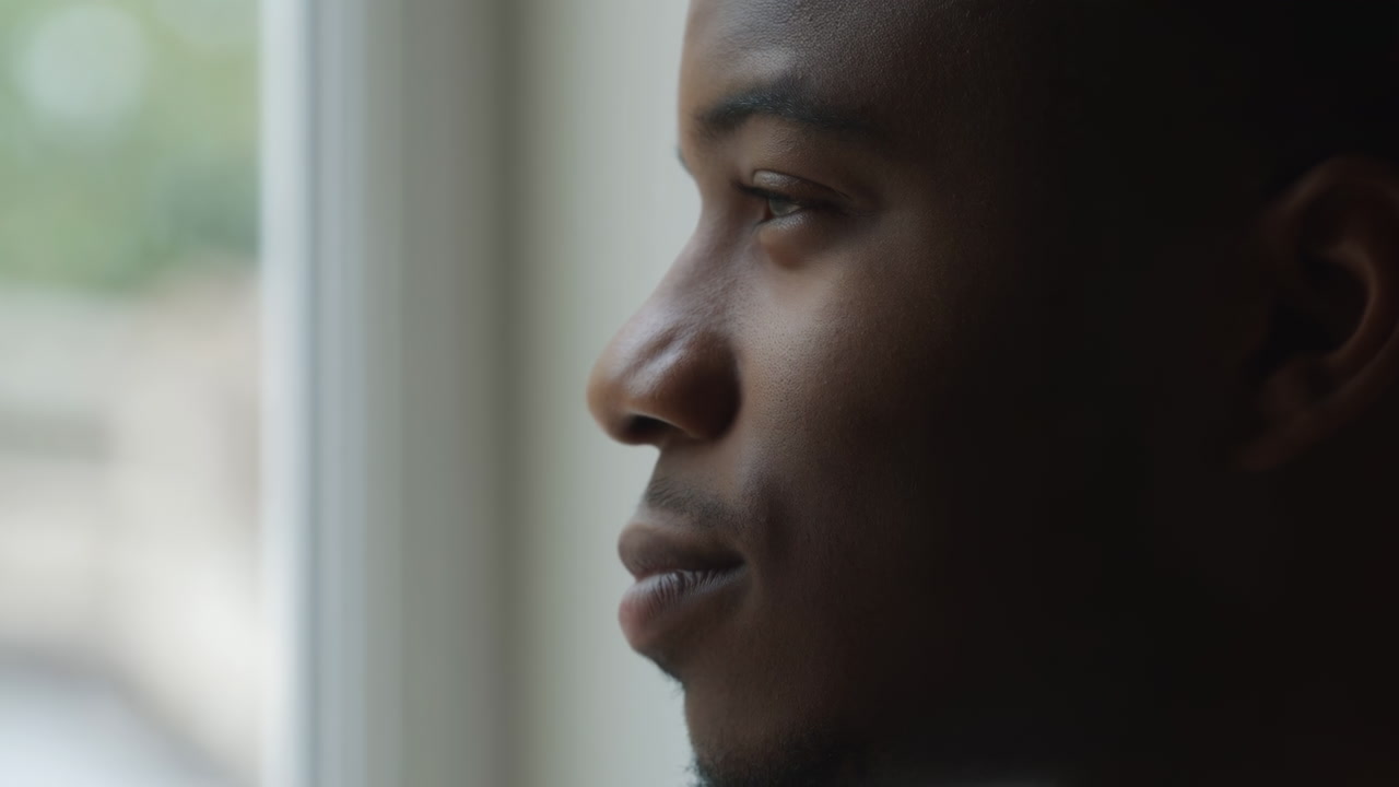 Black Man Gazing Out Window, Contemplative Young Adult Looking Through Soft Natural Light, Closeup Profile,