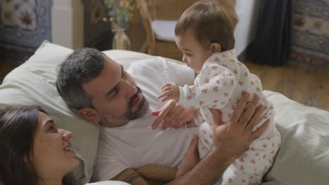 happy couple lying in bed on sunday morning and playing with their cute baby girl 1