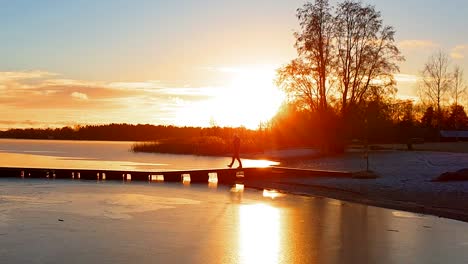 Silhouette-of-adult-male-talking-on-the-phone-in-lovely-arctic-scenery,-spectacular-sunset-in-the-background-and-long-shadows-on-ice-lake,-winter-time-in-early-December,-pan-and-tilt-follow