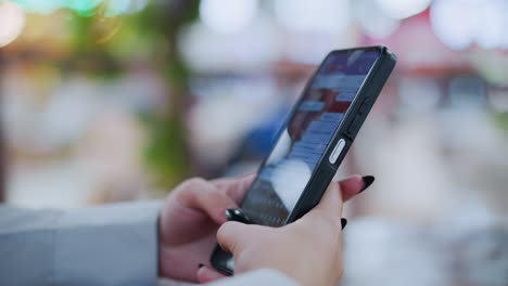 primer plano de la mano de la dama con uñas pintadas de negro hablando en el teléfono inteligente contra un fondo borroso suave y vibrante con luces bokeh, capturando un momento de interacción digital en un entorno moderno