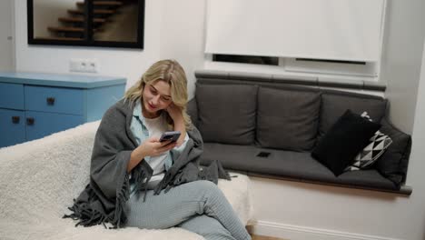 hermosa joven escuchando un mensaje de audio en un teléfono inteligente sentada en el sofá