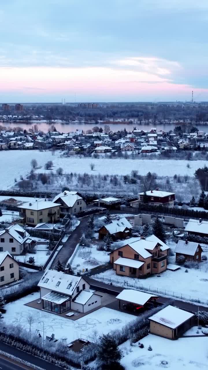 Aerial winter shot of a snowy neighborhood with a river winding through the landscape behind it - Vertical