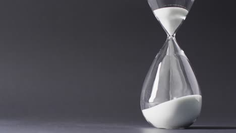 Video-of-close-up-of-hourglass-with-sand-pouring,-copy-space-on-black-background