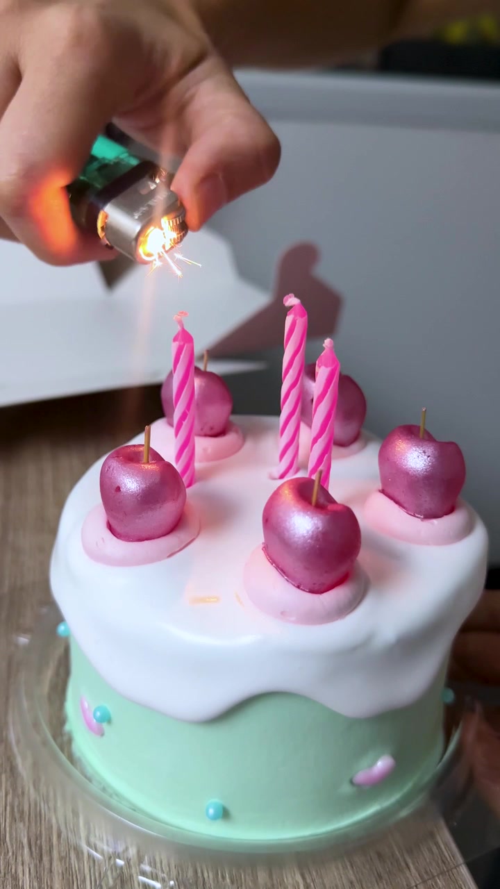 Una mano accende candele a spirale rosa su una torta decorata, ambiente interno, illuminazione naturale, primo piano.