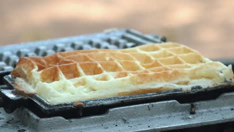 close shot of a waffle iron being opened with the waffle being removed with tongs