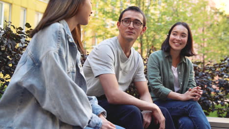 group of three young japanese friends talking together while sitting outdoors in the park