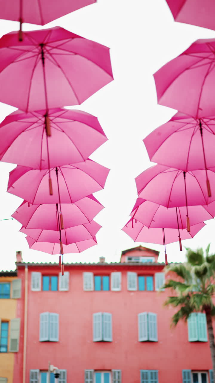 Rows of pink umbrellas above the streets of the old town in Grasse, France. Vertical