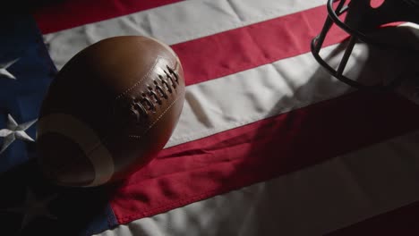 studioaufnahme einer person, die american-football mit helm auf der sternenbanner-flagge aufhebt