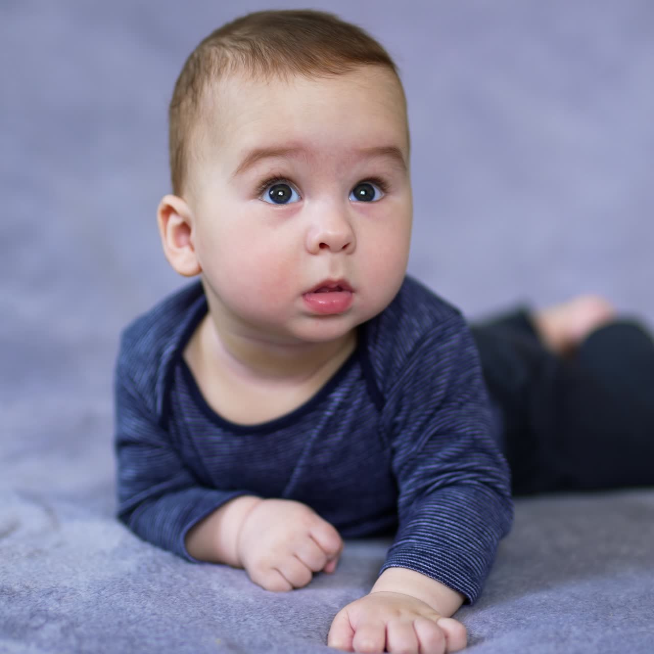 Lovely Caucasian child looks sideways with surprise. Astonished little kid watching something with an open mouth. Close up. Grey backdrop