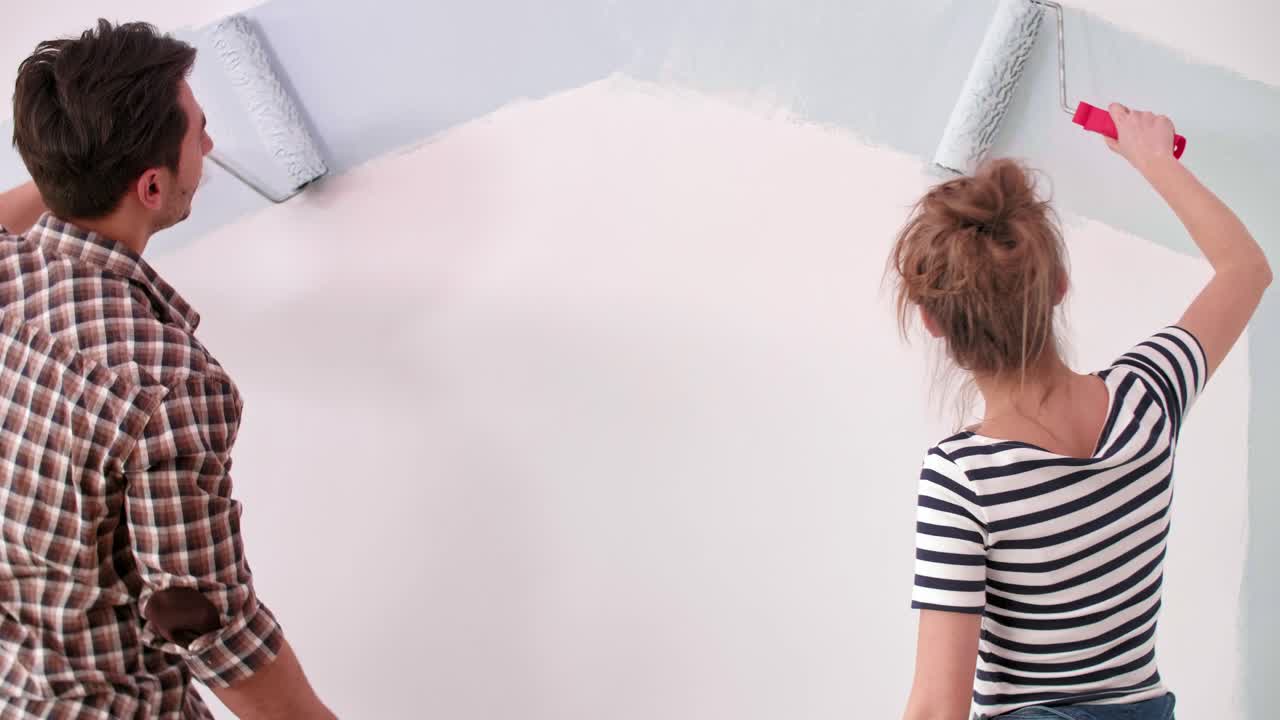 Pareja joven pintando la pared interior de su nuevo apartamento