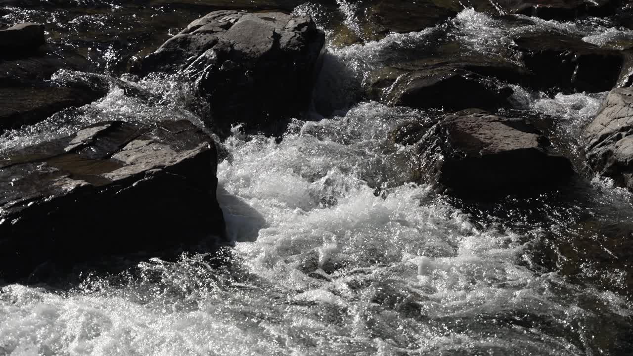 A flowing river glides over rocks, creating splashes and dynamic water patterns. slow motion