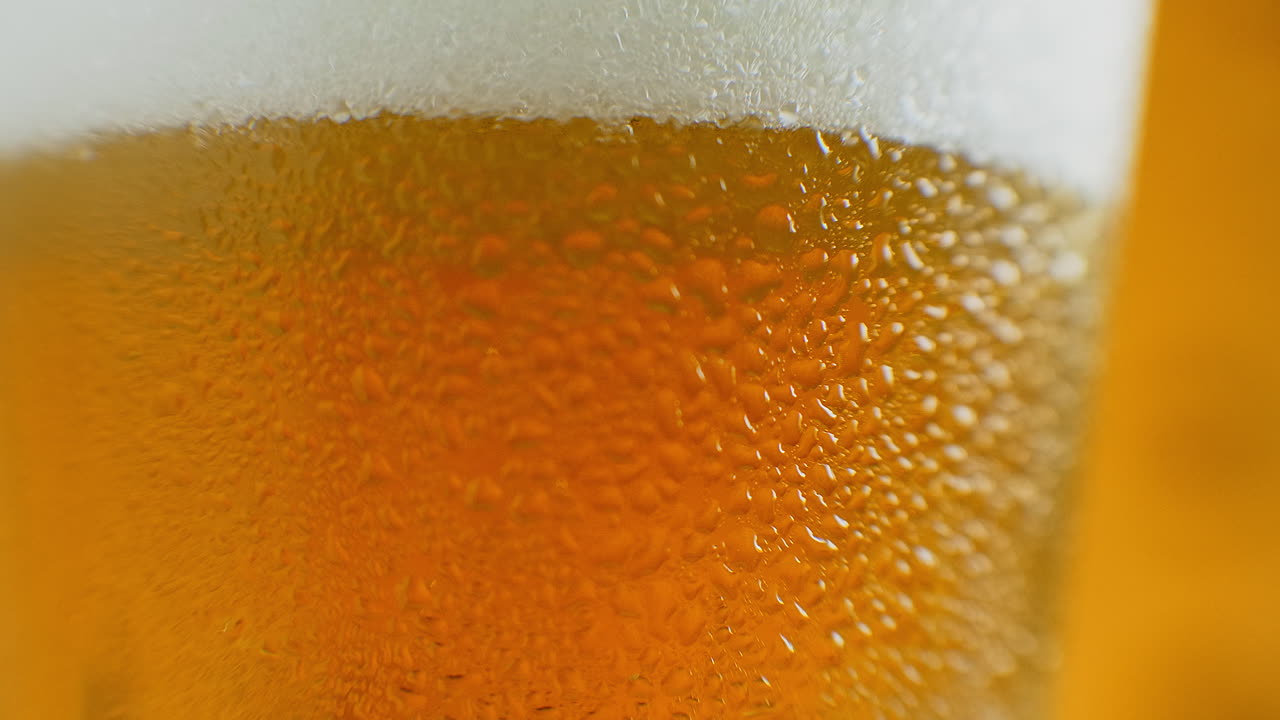 close-up cámara lenta: cerveza fría en un vaso grandes gotas y burbujas en la cerveza