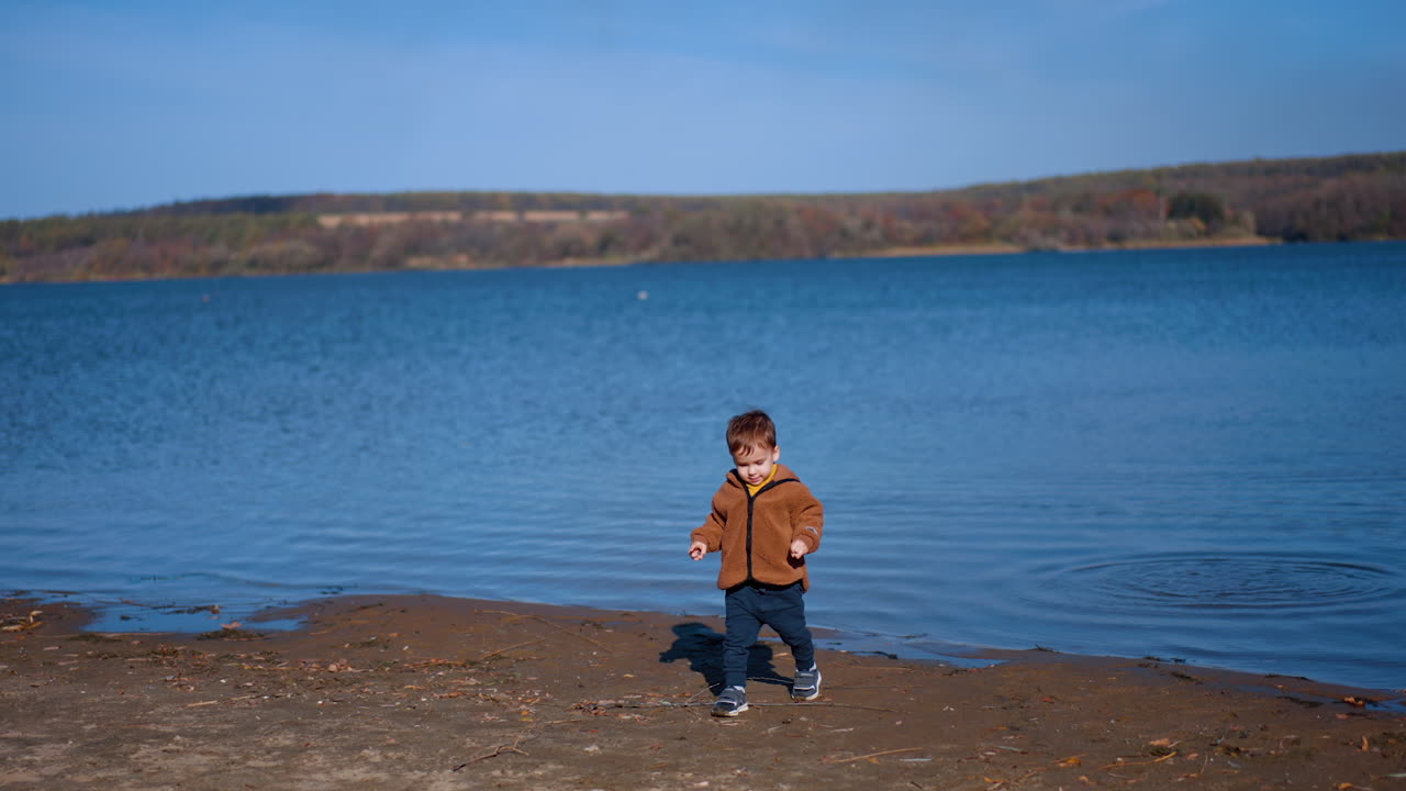 Baby boy having fun throwing stones into river. Kid cheerfully takes another stone and tossing into water.