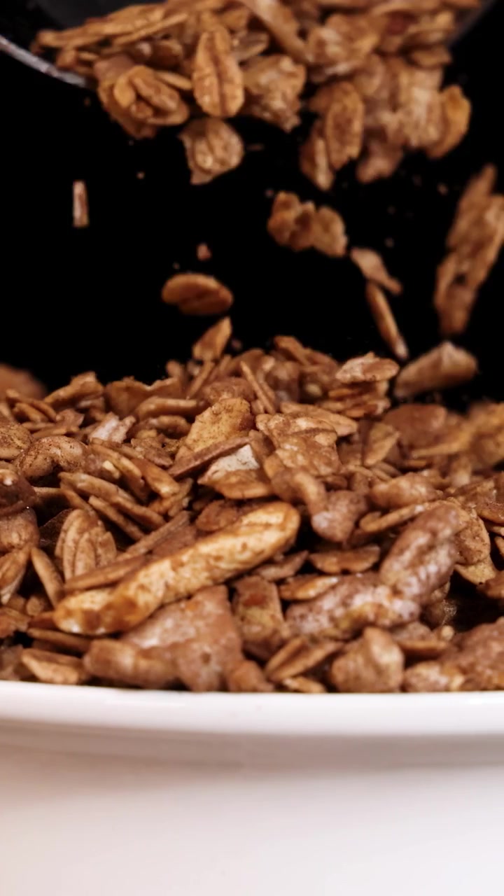 Pezzi di granola cadono in una ciotola, con un cucchiaio, su sfondo nero