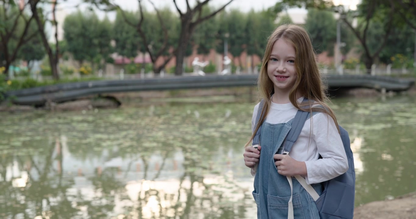 公園の池のほとりでリュックを背負って微笑む少女