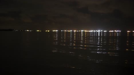 waves coming ashore with ship lights in the horizon at east coast park, singapore with rippling water that is very calm