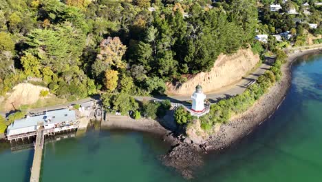 drone footage captures akaroa's scenic lighthouse, lush greenery, and turquoise waters under bright daylight