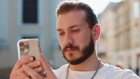 young man use smartphone typing text messages browsing internet finishing work looking at camera