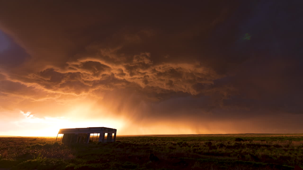 una tormenta supera una gasolinera abandonada mientras una puesta de sol ilumina el lado inferior de la tormenta
