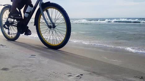 Man-Riding-Bicycle-On-Sandy-Beach-On-A-Cloudy-Day