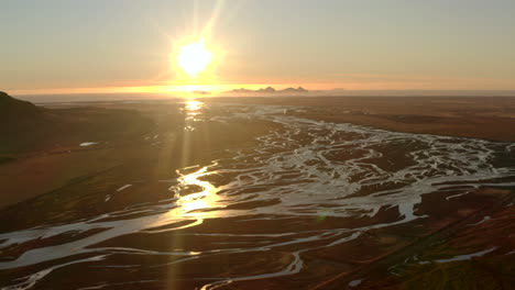 aerial shot over icelands braided rivers with the sunset and vestmannaeyjabær island in the background