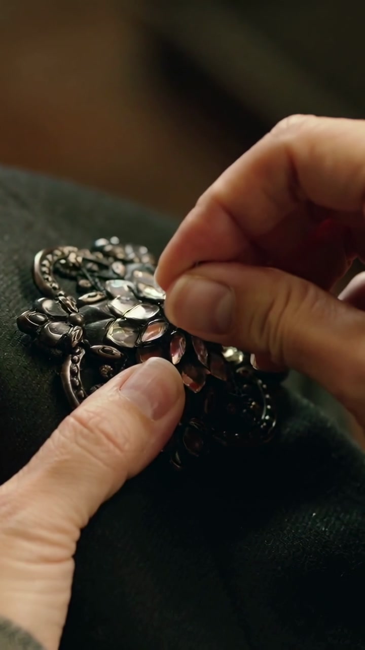 Vertical video: Positioning needle, senior hands tweaking brooch on dark cloth lap securing stones