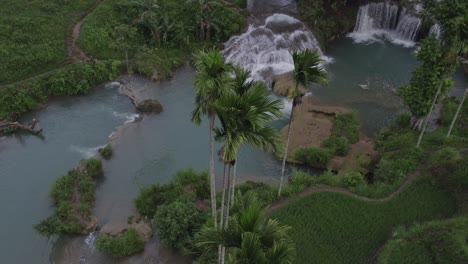 Drone-Vuela-Cerca-De-Palmeras-Junto-A-La-Cascada-Waikelo-Sawah-En-Sumba-Indonesia,-Aéreo