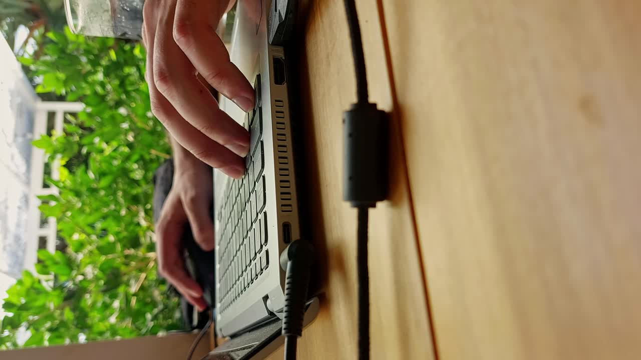 리조트에 있는 동안 노트북 키보드에서 타이핑하고 스크롤하는 바쁜 손의 수직 근접, 디지털 유목민 생활과 원격 작업의 솔직한 순간