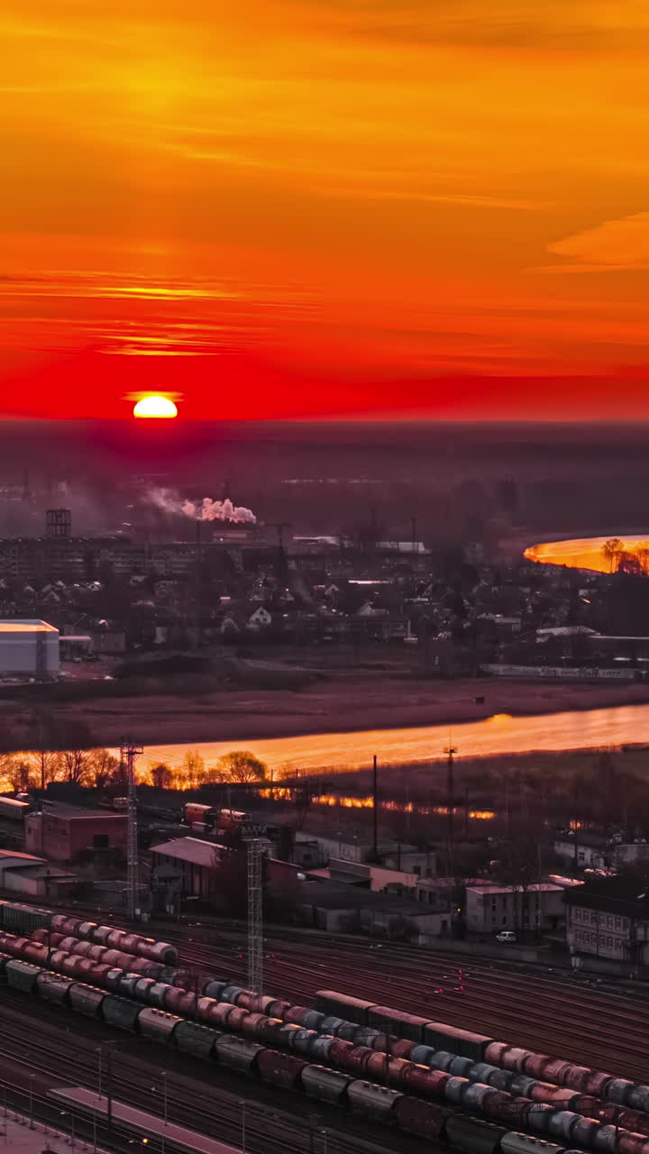 A stunning timelapse captures the fiery red and orange sunrise over the industrial city of Jelgava in Latvia, illuminating the sprawling railway yard with freight trains and a nearby river.
