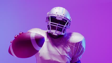 Video-of-african-american-american-football-player-with-ball-over-purple-neon-background