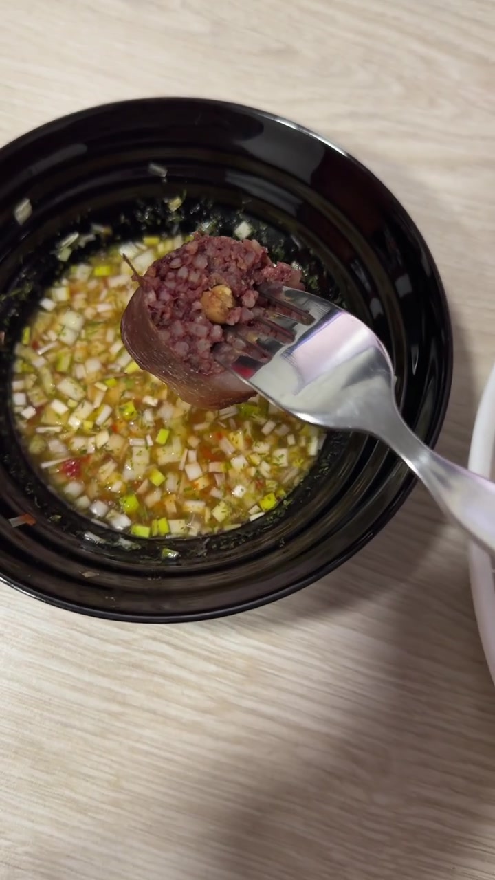 Fette verticali di morcilla cotta e patate novelle condite sono su un piatto accanto a una ciotola di salsa aji tritata su un tavolo di legno