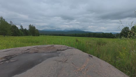 Ground level timelapse in the Adirondack Mountains of New York near Saranac Lake looking at high peaks with fast moving dark clouds and reflection from a small puddle on a large boulder
