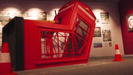 Red warped and distorted phone booth or a traditional telephone booth modern art sculpture made by Banksy at an exhibition. The object is sided by red traffic cones and lit beautifully, cinematically.
