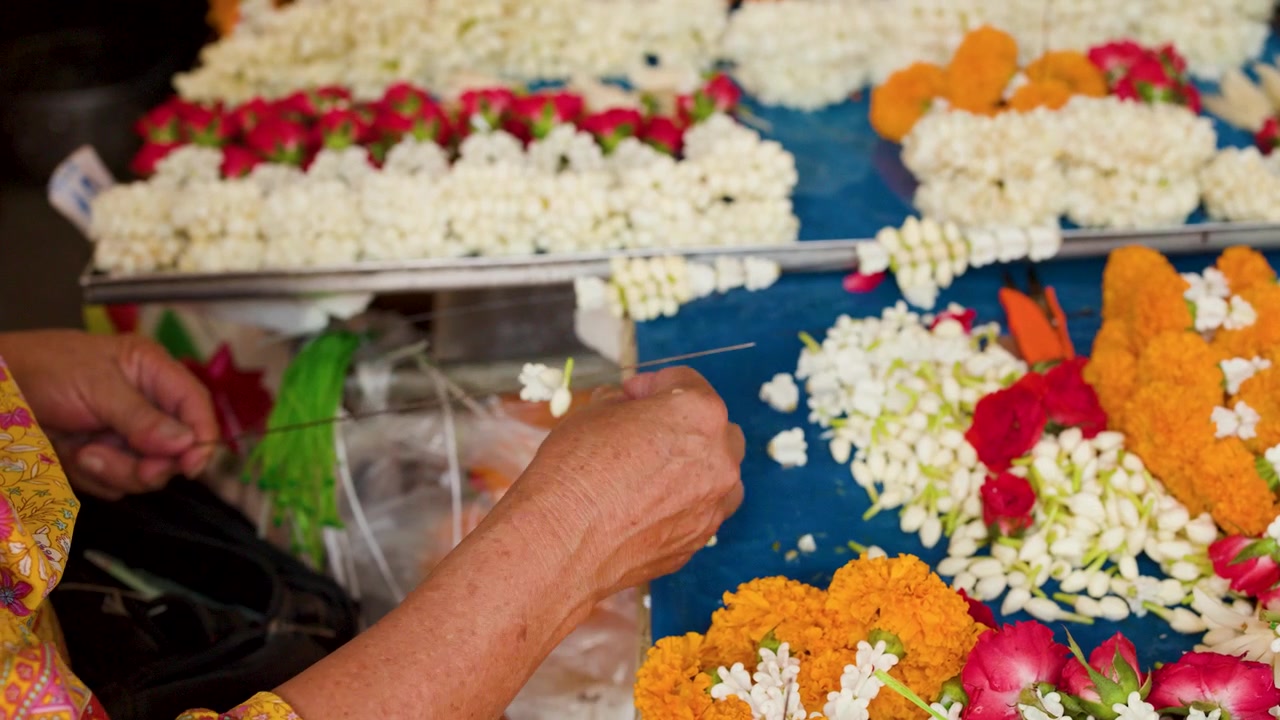 Primo piano di mani che infilano boccioli di gelsomino su un ago al Mercato dei Fiori di Bangkok, Thailandia