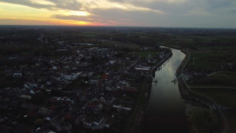 Aerial-backwards-view-of-small-city-along-the-river-at-sunset