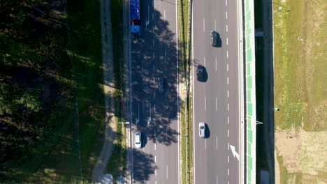 Top-down-view-of-a-road-with-moving-car,-contrasting-shadows,-and-adjacent-greenery