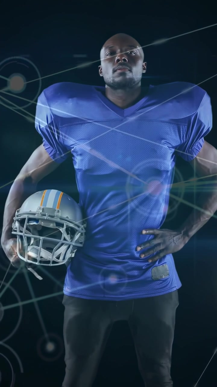 Jogador posando em estúdio, com camisa azul e ombreiras, segurando capacete prateado com hologramas.