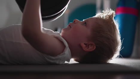 Focused-little-boy-lifts-heavy-barbell-at-bright-light