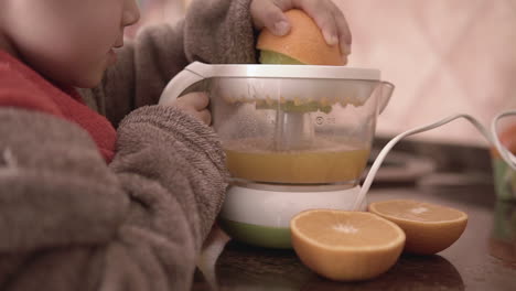 little kid learning how to use the electric squeezer to make fresh orange juice