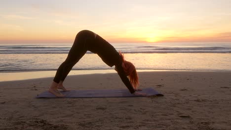 woman on the beach performing dog pose practicing yoga at sunrise