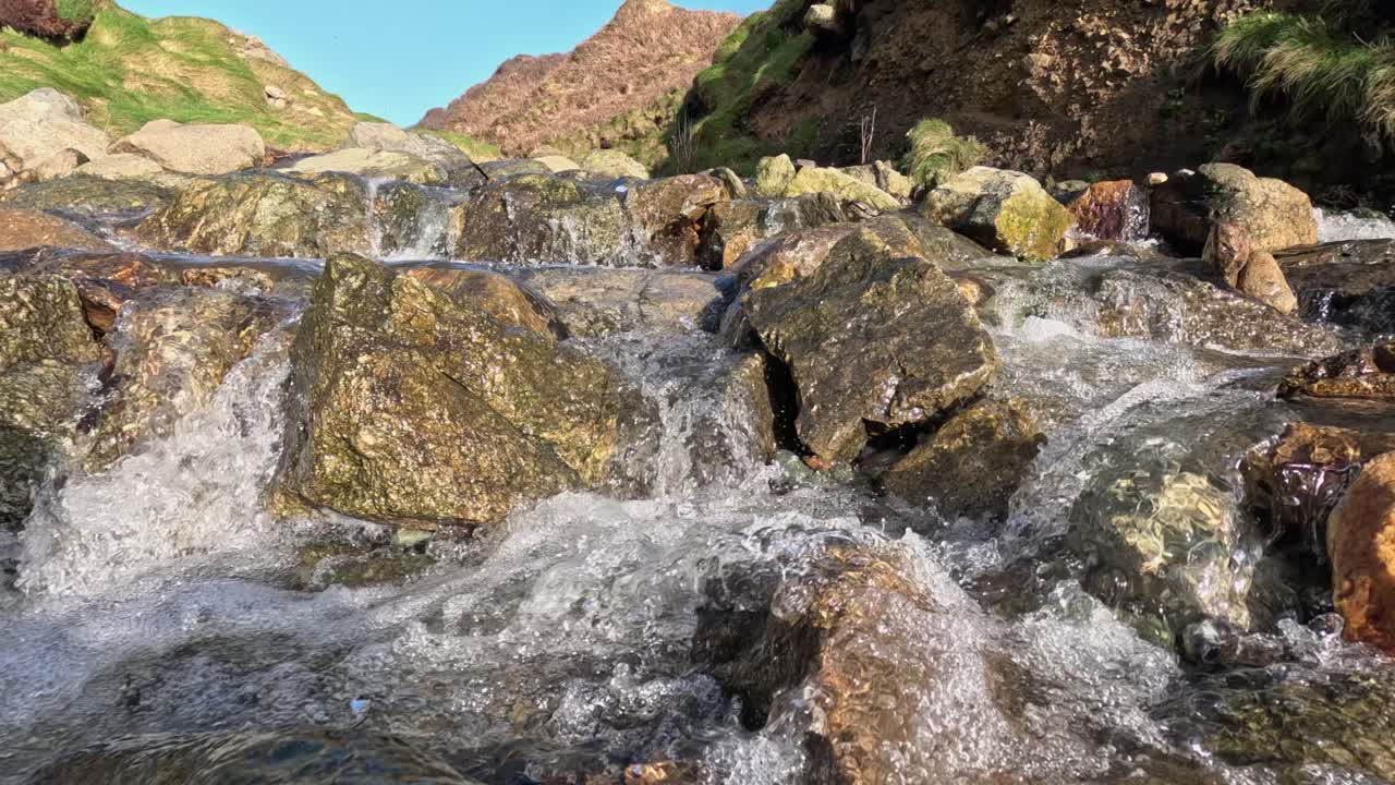 Crisp, clear mountain river water cascades down rocky falls, closeup