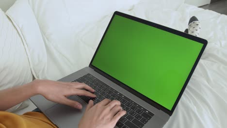una mujer usando una computadora portátil con una pantalla verde en la cama de su casa.