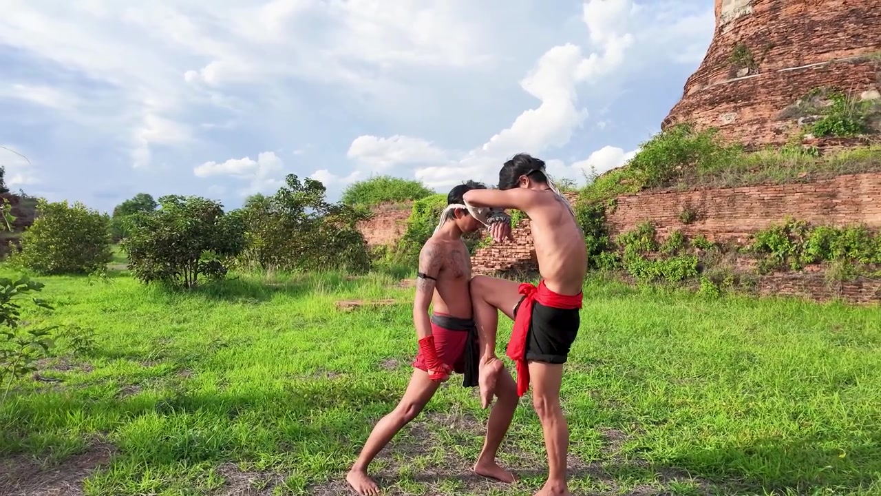 To traditionelle thailandske kickboksere øver knæspark udendørs ved det historiske tempelområde Ayutthaya