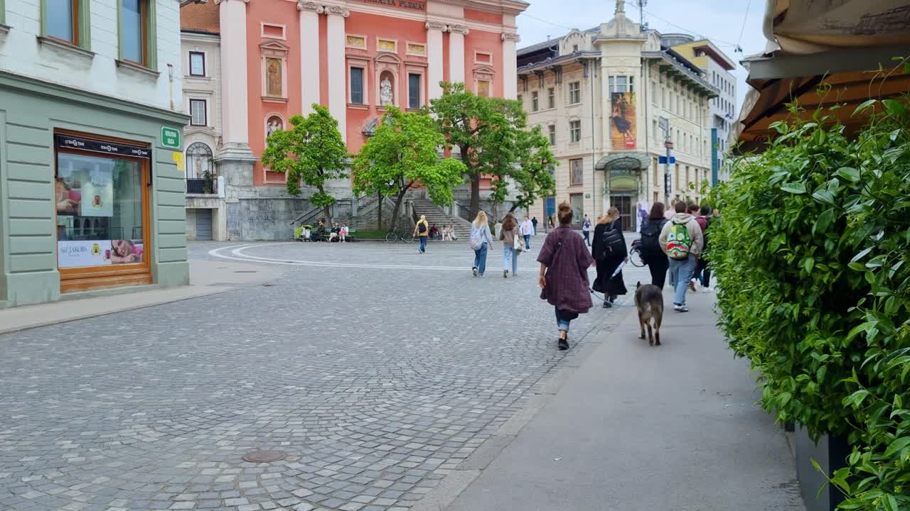 Locals, tourists, cyclist and dog owner passing in front of the Church of the Annunciation or Franciscan Church on Preseren square in the center of Ljubljana Slovenia on an cloudy spring day