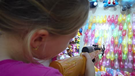 Joven-Caucásica-Disparando-Una-Pistola-De-Balas-De-Goma-En-Filas-De-Globos-Coloridos-Para-Ganar-Premios-En-El-Campo-De-Tiro