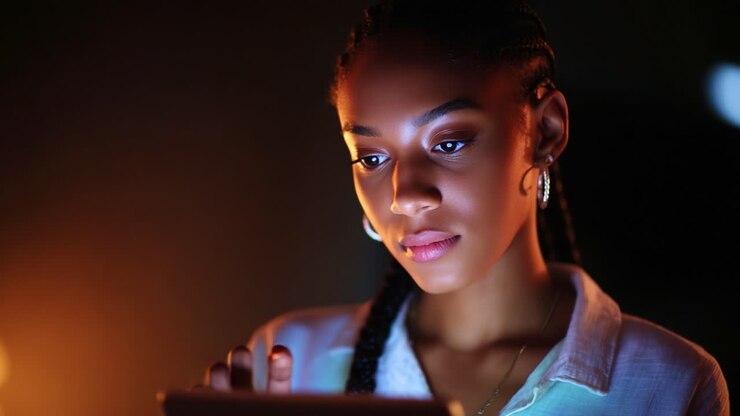 Captivating Moment of Focus: A Young Woman Engaged Deeply with a Digital Device, Illuminated by a Soft Glow in a Dimly Lit Environment, Showcasing Her Intense Concentration and Calm Demeanor