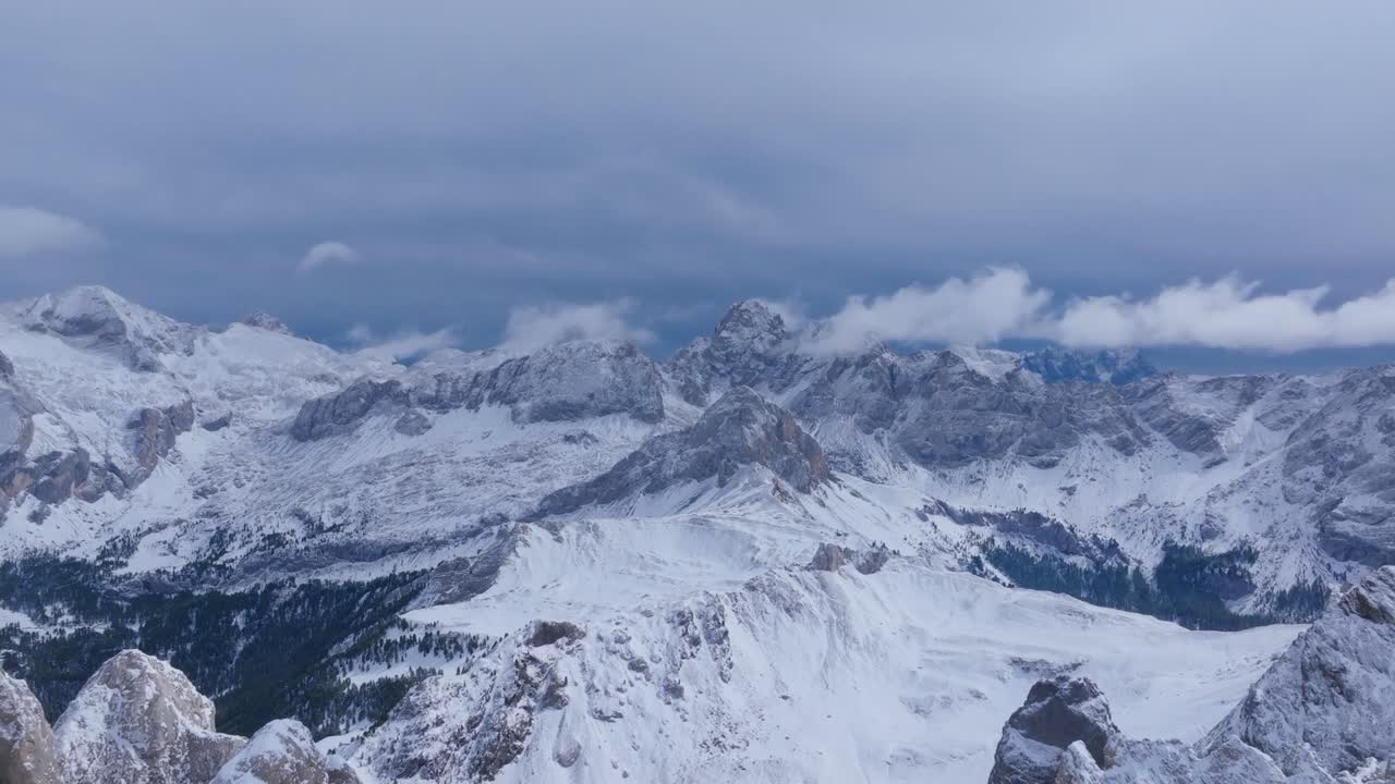 Aerial drone shot showing wide view of snow covered mountain range with rugged peaks, cloudy sky, and forest patches in West Virginia, America, during cold winter season in remote wilderness